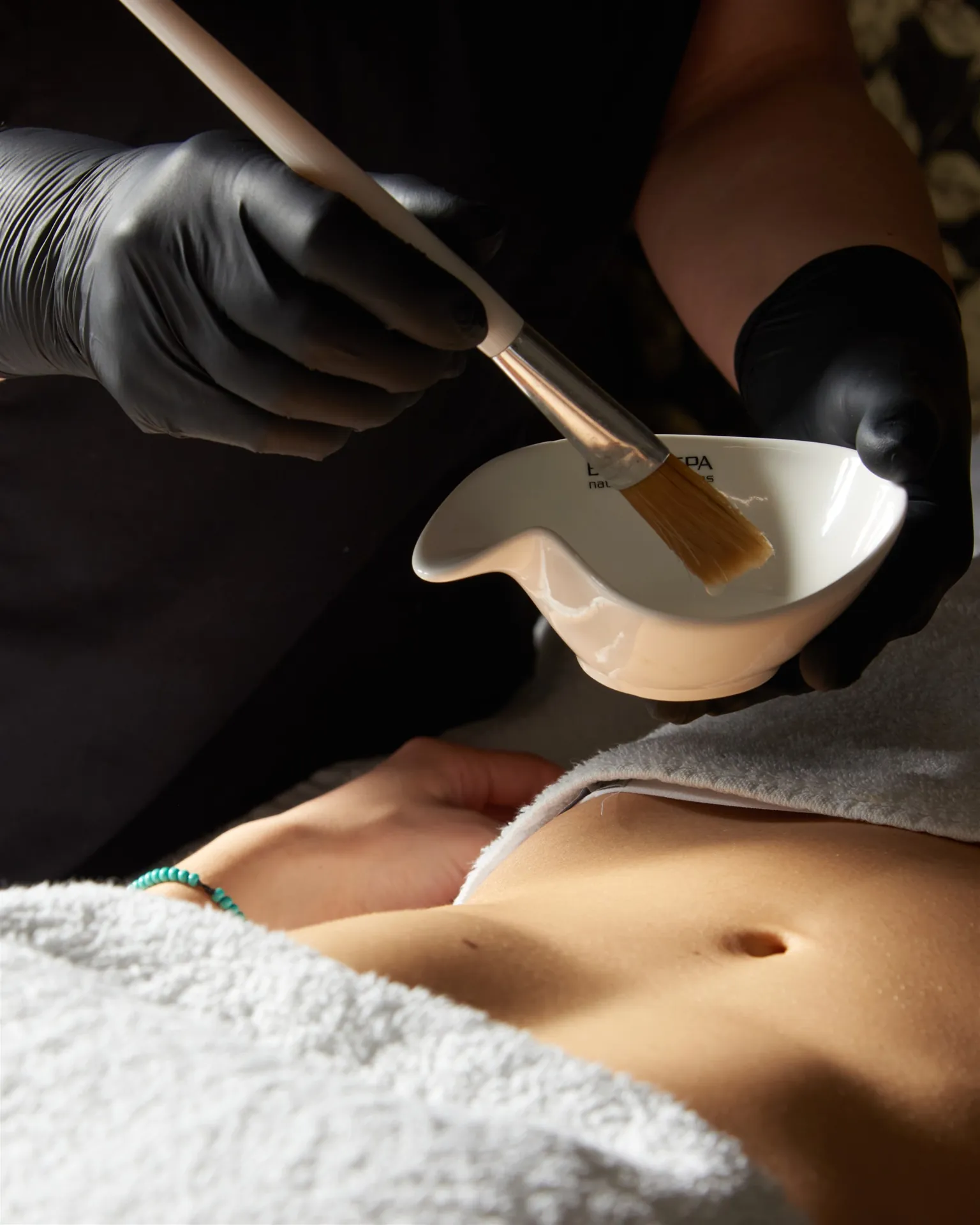 Operatrice Jêtre applica con il pennello un attivo professionale durante un trattamento corpo